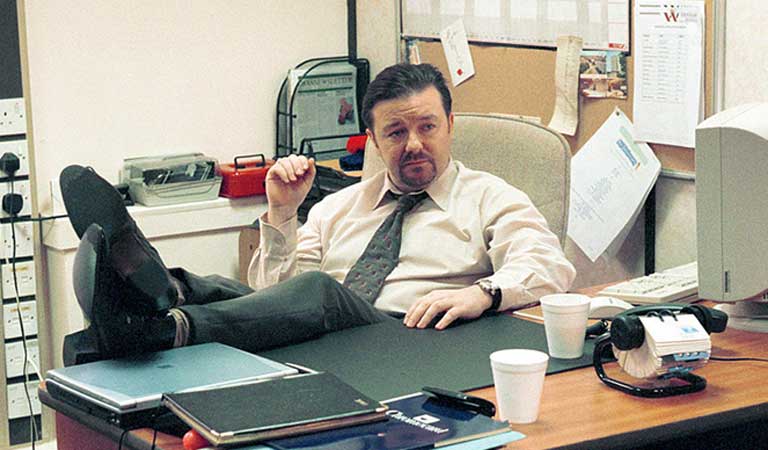 Ricky Gervais sitter ved en pult