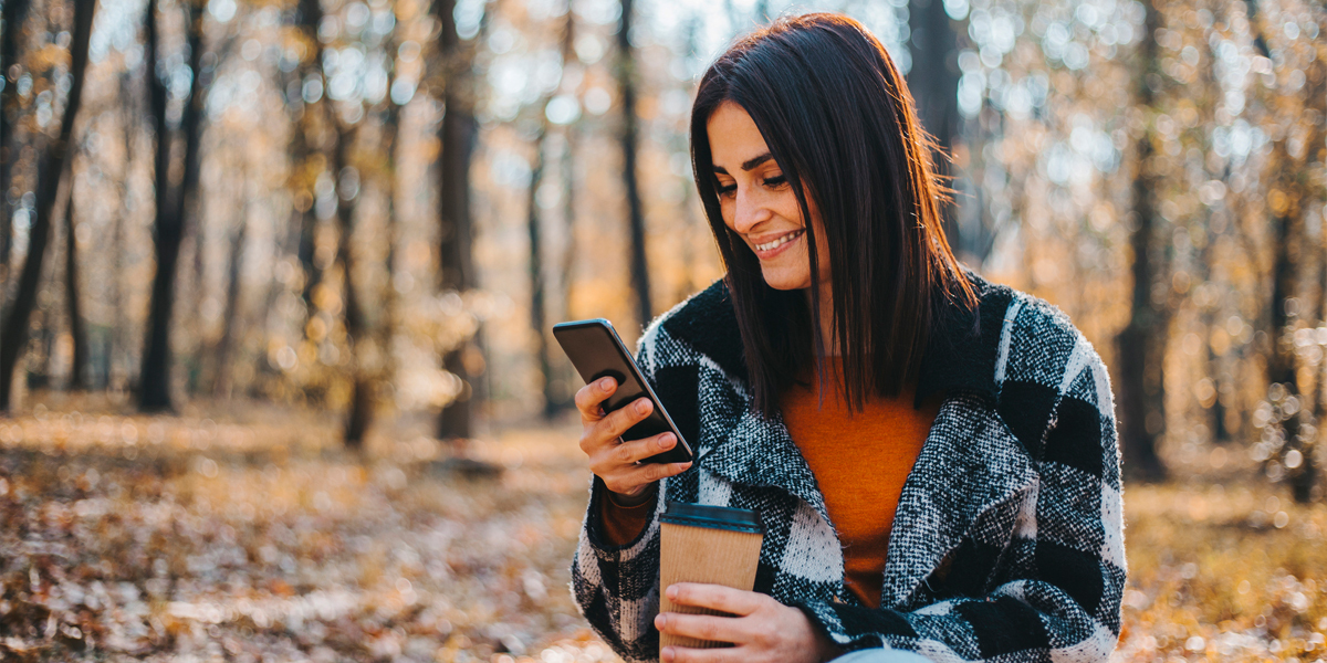 kvinne bruker mobil i skogen om høsten