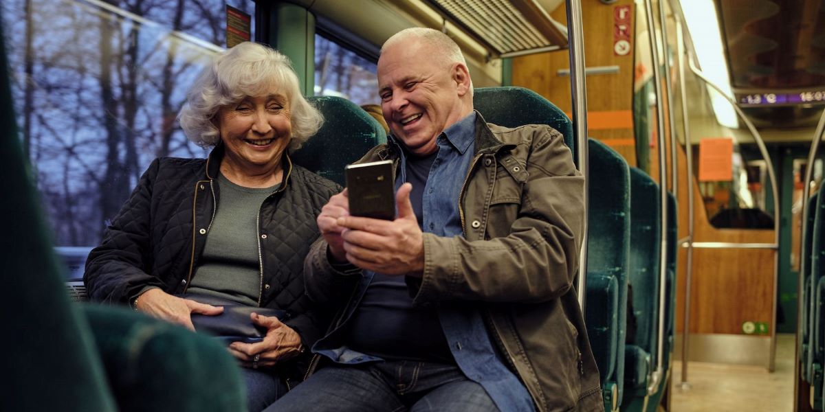 Eldre par på buss som gleder seg over god dekning og høy fart på mobilen takket være Norges beste mobiloperatør