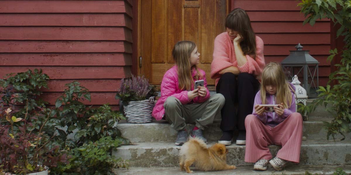 Bilde som viser mor, to døtre og en hund sitte på trappen utenfor inngangsdøren til rekkehuset.