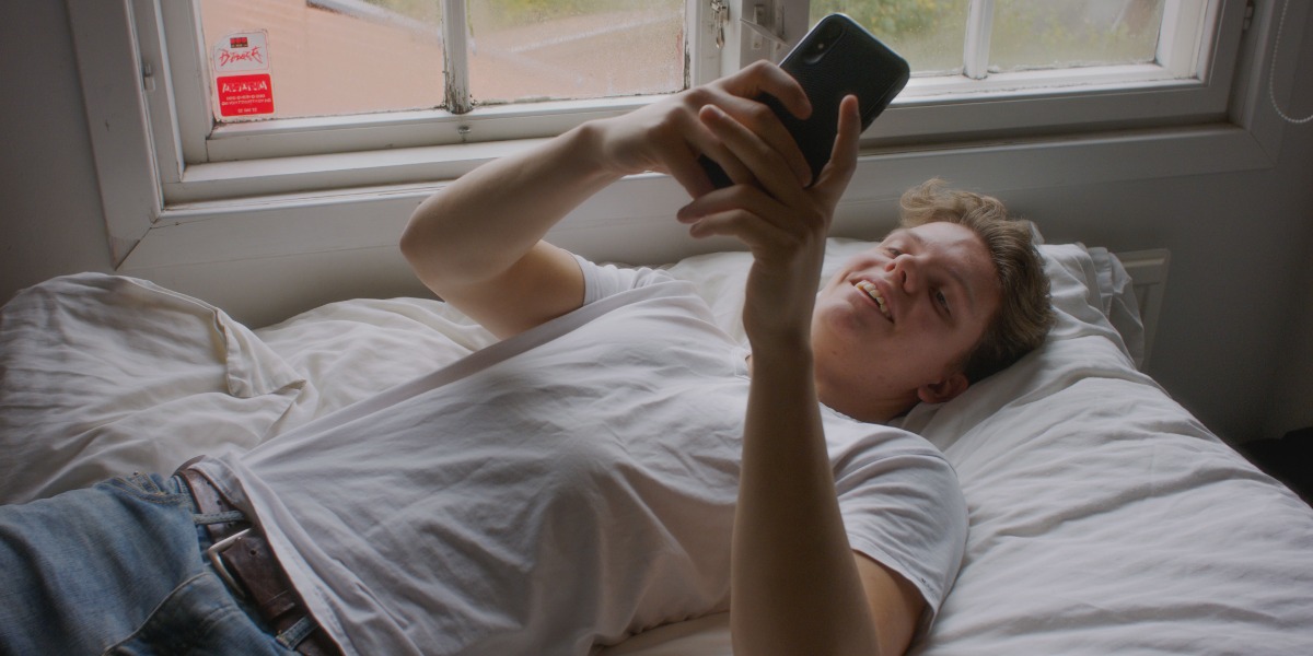 Bilde av gutt som ligger på ryggen i senga med smarttelefon i begge hender