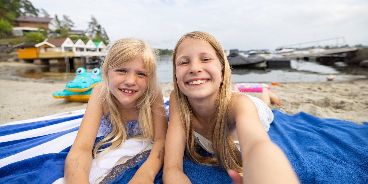 Sommerminne: to søstre som tar selfie mens de ligger på et badehåndkle på stranda