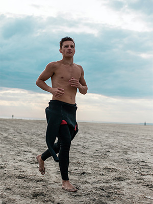 Mann som løper på strand i bar overkropp