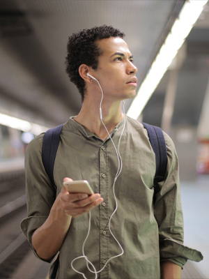 mann på togstasjon med mobil og øreplugger